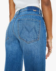 A person shown from the back wears Mother’s The Dodger Ankle jeans—high-waisted, loose straight leg, blue with a large "M" stitched on the back pocket—paired with a white top and one arm relaxed at their side.