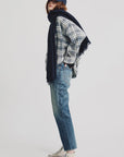 A person wears the Denimist CROPPED BUTTON FRONT SHIRT with blue jeans, white sneakers, a navy scarf, and a navy baseball cap, standing sideways with hands in pockets against a plain white background.
