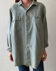 A person wears Red Vintage Co.'s 1950s Sage Canvas Workshirt—an oversized light gray-green heavyweight shirt coat with chest pockets—paired with blue jeans, standing against a plain light background.