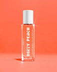 A clear glass bottle of Faire Heretic 15ML Perfume with a white cap and bold white text stands upright on a peach-colored background, evoking sandalwood and vanilla notes.