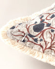 A close-up of Faire's Block Print Pillow shows cream fringe edges, a blue and brown floral pattern, and a small metal zipper pull along the seam of this vintage-style decorative pillow.