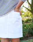 Outdoors, someone wears the Frank & Eileen Jameson Skirt with utility pockets and a mid-rise fit, paired with a black-and-white striped top and hand in the pocket. Green foliage and blurred flowers are visible in the background.