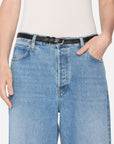 A person wearing FRAME’s The Pixie Loose light blue rigid denim jeans with a black leather belt and a white ribbed tank top, hands in front pockets. Image is cropped to show torso and upper legs, highlighting the jeans’ wide-leg fit.