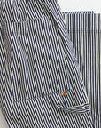 A close-up of the Indigo Stripe Sailor Pant by Free City (sparrow, LLC), featuring unisex blue and white vertical stripes, a front pocket with black button, and a small red and white "FRY ONE" tag on the seam.