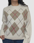 A woman wears the White + Warren Cashmere Argyle Crew in cream with beige, brown, and red accents, paired with blue jeans. The sweater has a round neckline and long sleeves, shown against a plain white background.