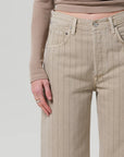 A person wears the Ayla Raw Hem Crop by Citizens Of Humanity/AGOLDE: beige, high-waisted, wide-leg pinstripe pants in heavyweight non-stretch cotton. Only their lower torso and one hand are shown against a plain light background.
