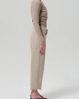 A person stands in profile against a light background, wearing a fitted beige long-sleeve top and high-waisted Citizens Of Humanity/AGOLDE Ayla Raw Hem Crop pinstripe pants in heavyweight non-stretch cotton with black heeled sandals.