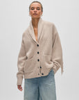 A model in light blue jeans and the White + Warren Cashmere Blend Luxe Fringe Coatigan, a beige merino wool-cashmere button-up cardigan with large front pockets, thick collar, and fringe sleeves, poses against a plain white background.