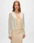 A woman with long, light brown hair wears a White + Warren Superfine Cashmere Cardigan over a cream sleeveless dress, standing against a plain white background.