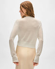 A woman with wavy brown hair is seen from behind in a White + Warren Superfine Cashmere Cardigan and matching cream skirt, set against a plain light background.