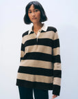A woman with a short bob wears the White + Warren Cashmere Rugby Stripe Polo in beige and brown stripes with dark pants, standing against a light background.