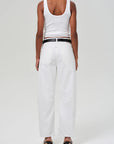 A person, back to the camera, wears a white tank top, Citizens Of Humanity/AGOLDE Miro relaxed fit jeans with a black belt, and black heeled sandals. Set against a plain white background.