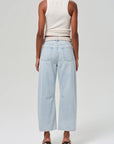 A person is seen from the back wearing the Miro white sleeveless top and light blue barrel leg jeans by Citizens Of Humanity/AGOLDE. They stand on a light gray background and wear heeled sandals.