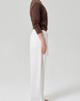 A person stands sideways against a plain background wearing a long-sleeve brown shirt and the Citizens Of Humanity/AGOLDE aurora pull on pant—a loose-fitting, soft cotton flax blend women’s pant with front pockets. Their left arm is relaxed, feet bare.