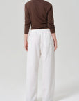 A person stands facing away, wearing a long-sleeved brown top and the Citizens Of Humanity/AGOLDE aurora pull on pant—loose-fitting with an elastic waistband in a cotton flax blend—against a plain light gray background.