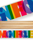 A rectangular Long Safety Matches box by Faire features bold, colorful "MAGNIFIQUE" lettering on the lid and side in red, blue, orange, pink, purple, green, and yellow. The open box reveals wooden matches—perfect for unique match box designs.