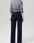 A person faces away from the camera, wearing a gray ribbed sweater over a white long-sleeve top and Citizens Of Humanity Annina Pocket Trouser in dark indigo—a high-rise, wide-leg denim style—against a plain light background.