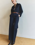 A person stands against a white wall wearing the Annina Pocket Trouser by Citizens Of Humanity/AGOLDE, crafted from recycled cotton. Styled with a brown belt and pointed-toe boots, they pose casually with hands in pockets.