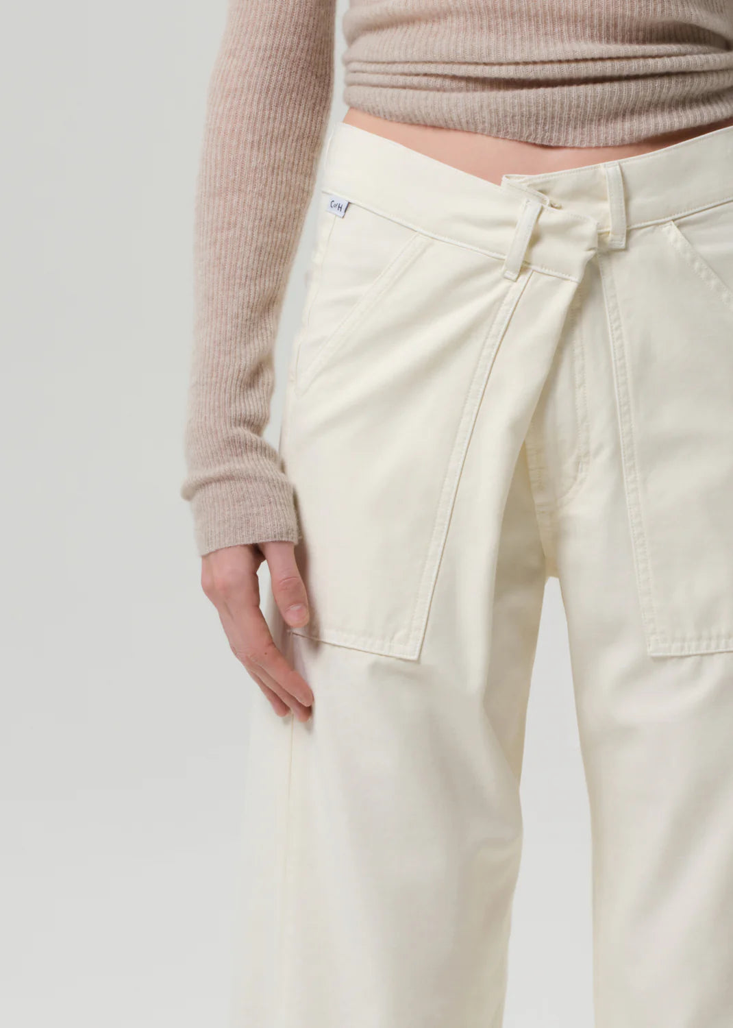 A model wears the Citizens Of Humanity/AGOLDE Ines Crop Utility Trouser—off-white, high-rise, cropped with a front flap and utility pockets—paired with a beige ribbed long-sleeve top, shown from mid-torso to thigh on a plain light background.