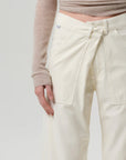 A model wears the Citizens Of Humanity/AGOLDE Ines Crop Utility Trouser—off-white, high-rise, cropped with a front flap and utility pockets—paired with a beige ribbed long-sleeve top, shown from mid-torso to thigh on a plain light background.