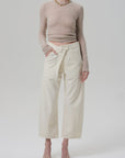A person wears the Ines Crop Utility Trouser by Citizens Of Humanity/AGOLDE—high-rise, cropped, regenerative cotton twill with utility pockets—paired with a fitted long-sleeve beige crop top and open-toe heeled sandals against a plain background.