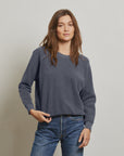 A woman with long brown hair wears the Perfectwhitetee Ziggy Reverse LS Sweatshirt and blue jeans, standing against a light gray background and looking at the camera with a neutral expression.