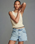 Wearing the FRAME Bauble Tank, a person poses with one arm raised and the other crossed over, styled with frayed denim shorts against a plain gray background.