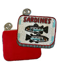 The image shows two small coin purses by Faire: one plain red, and the "Beaded Sardine Tin Coin Purse" featuring handmade beading of two sardines with “SARDINES” above. Both have circular jeweled clasps for extra charm.