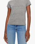 Dressed in Mother’s The Lil Goodie Goodie Tee in heather gray with a crewneck, blue jeans, gold layered necklaces, bracelet, and rings, a person stands against a plain light background for an effortless vintage style.