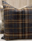 Two TL At Home Durrell Pillows 24X24, featuring brown, gray, and white plaid wool stripes, rest on a light-colored sofa. The front pillow is in focus; the one behind is slightly blurred.