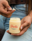 A person in blue jeans and a belt scoops Not specified Magnesium Cream from a jar, dipping their hand into the rich blend of essential oils and beef tallow.