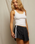 A woman with wavy blonde hair wears a lightweight white tank top and Perfectwhitetee’s Mikayla Travel Short, radiating sporty energy as she stands against a neutral background.