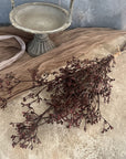 The Faire 22'' Faux Seeded Baby's Breath Bunch, tied with twine, is displayed on a textured beige surface next to a vintage metal pedestal dish and sheer brown fabric.