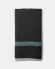 The Faire CH Tea Towels S/2 showcases a dark gray folded tea towel with a teal stripe near one end and a light gray accent along the bottom edge, inspired by Antibes style, displayed against a plain white background.