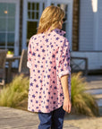 A person with blonde hair, wearing sunglasses and blue pants, models the Frank & Eileen Eileen S25 relaxed fit long-sleeved shirt with a pink and purple star pattern outdoors near a patio and greenery.