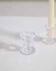 The Bellamy Candleholder by Accent Decor, in clear glass and urn-shaped, sits on a white surface beside its matching taper holder with a pale yellow candle.
