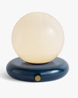 The Valencia Portable Light by Faire features a round frosted white glass globe on a glossy dark blue circular base with a small gold-colored button, offering a sleek and minimalist design.
