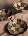 Hand-finished checkered travertine bowl by The Faire on beige fabric, classic accent for living or dining spaces.
