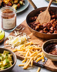 A wooden board with shredded cheese, diced avocado, seasoned taco meat, salsa, lime wedges, and a jar of Faire Taco Seasoning adds bold Southwestern flavor to this fresh tortilla wrap spread.