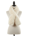 The Faire Lamb Fur Pull Through, a cream-colored, fluffy scarf, is styled in a crisscross on a beige dress form with black stand and finial, radiating luxurious warmth.