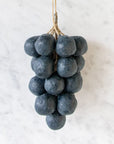 Handcrafted Grapes Soap by Faire, resembling a cluster of dark grapes, hangs by twine against a white marble background for an artisanal touch.