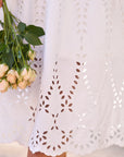 A person in the Frank & Eileen Gracie Midi Eyelet Dress with intricate cut-out embroidery along the hem holds a small bouquet of pale peach roses.