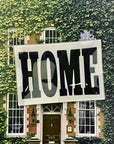 The Faire Home Block Glass Tray features vintage "HOME" typography in bold black, perfect for displaying against house exteriors with green ivy, brickwork, large windows, and a central dark door.