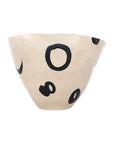 The Clyde Bowl by The Import Collection is a beige, asymmetrical porcelain piece with black irregular circular and oval shapes, creating a striking modern centerpiece against a white background.