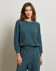 A woman with long brown hair wears a textured teal Ziggy Reverse LS Sweatshirt by Perfectwhitetee with bracelet-length sleeves and matching sweatpants, standing against a plain light background.