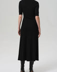 A person wearing the Citizens Of Humanity/AGOLDE Amina Polo Dress with black knee-high boots stands facing away from the camera against a plain, light background.