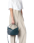 A person in a white t-shirt and beige wide-leg pants holds the Jerome Dreyfuss Pepito Medium Bag, featuring a quilted leather handle and adjustable strap. The image highlights the outfit and handbag against a plain white background.