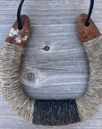 The Lucky Horseshoe by Faire features a U-shaped upcycled horseshoe with rusted ends, wrapped in coarse tan and black twine, hanging on a black cord—ideal rustic decor for your home.