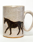The Faire Ceramic Mug is a textured, handmade piece featuring a silhouette of a walking horse. It is dishwasher-safe with a predominantly beige color and brown speckles, while the horse design is in dark brown.