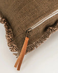 Close-up of the Luxe Linen Lumbar Pillow by Faire, a brown textured pillow with fringed edges, visible white zipper, and brown leather pull tab, shown on a plain white background.